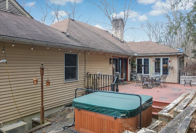 rear view of property featuring roof with shingles, a wooden deck, outdoor dining area, a chimney, and a hot tub