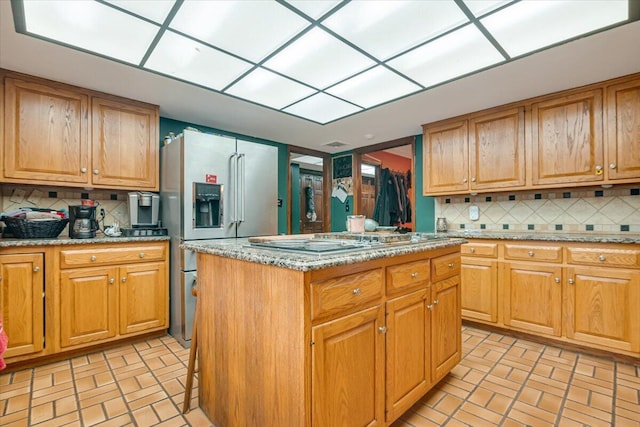 kitchen featuring light stone counters, stainless steel fridge with ice dispenser, tasteful backsplash, and a center island