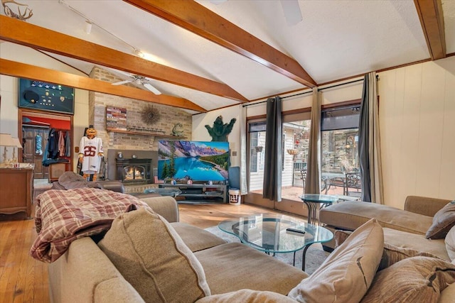 living room featuring lofted ceiling with beams, wood finished floors, a wood stove, and ceiling fan