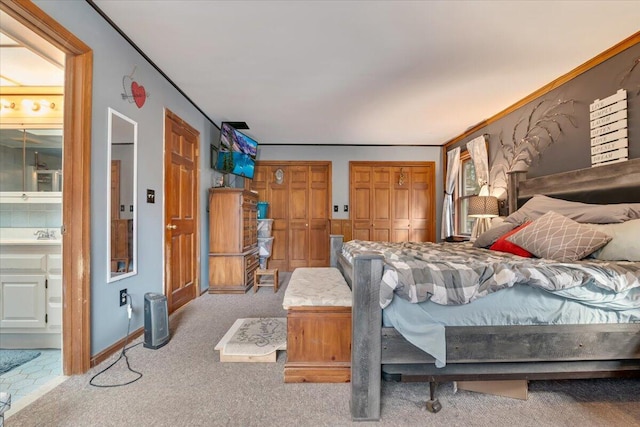 bedroom featuring ornamental molding, ensuite bathroom, multiple closets, and carpet floors