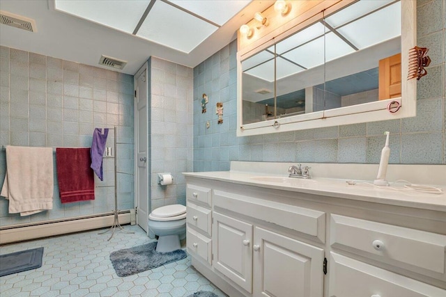 bathroom with visible vents, toilet, vanity, baseboard heating, and tile walls