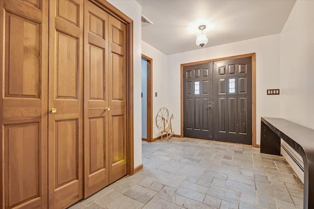 entrance foyer featuring stone tile flooring, baseboard heating, visible vents, and baseboards