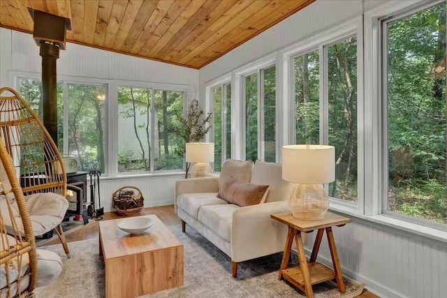 sunroom with a ceiling fan, wooden ceiling, a wood stove, and vaulted ceiling