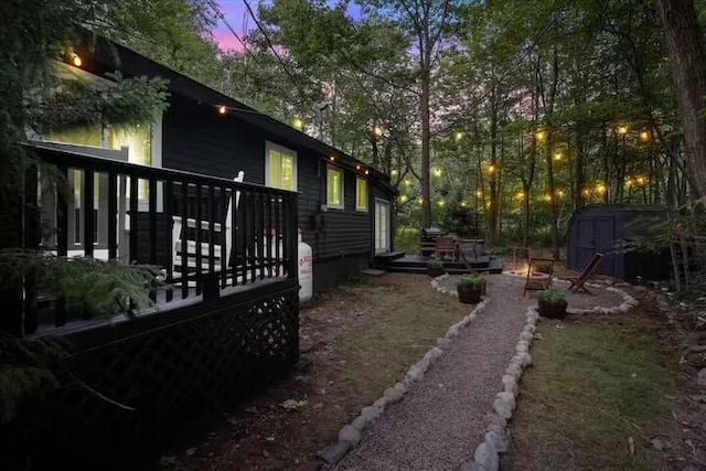 view of side of property featuring a wooden deck, an outdoor fire pit, a storage unit, and an outdoor structure