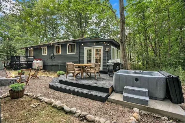 rear view of house featuring a deck, a fire pit, french doors, and a hot tub