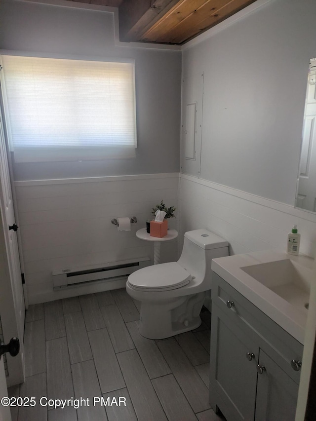 half bathroom with wainscoting, toilet, wood tiled floor, vanity, and a baseboard heating unit