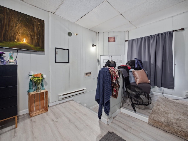 interior space featuring wood finished floors, a drop ceiling, and a baseboard radiator