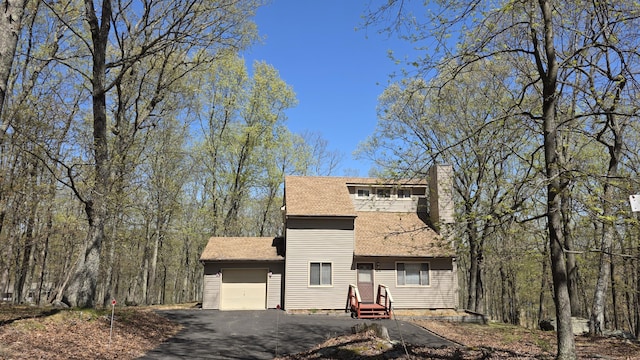 view of front of house featuring a garage, aphalt driveway, a chimney, and a shingled roof