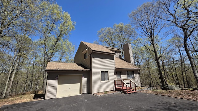 view of front of home featuring driveway, a chimney, roof with shingles, and a garage