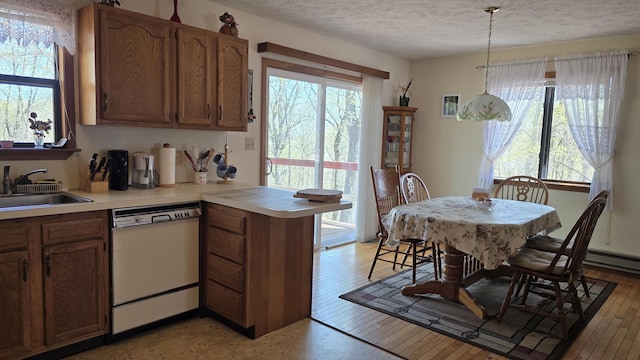 kitchen with a sink, dishwasher, light countertops, a textured ceiling, and a peninsula