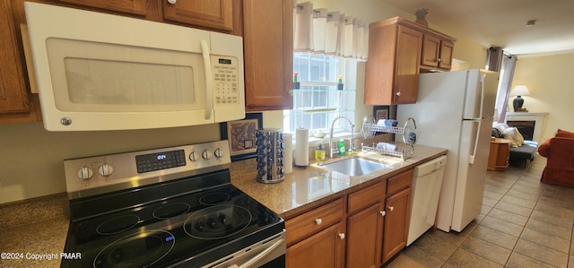 kitchen featuring stone counters, tile patterned flooring, white appliances, a sink, and brown cabinetry