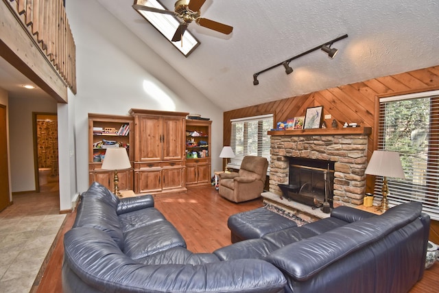 248 Miller Dr, Pocono Pines, PA 18350 - living room featuring wood walls, a stone fireplace, rail lighting, high vaulted ceiling, and ceiling fan