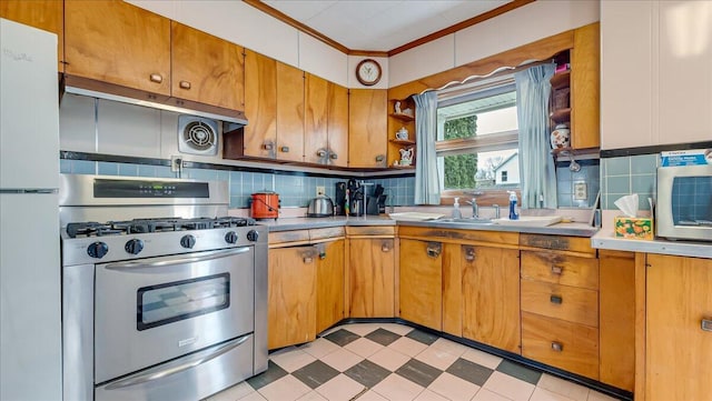 kitchen featuring stainless steel gas range oven, light floors, light countertops, decorative backsplash, and freestanding refrigerator