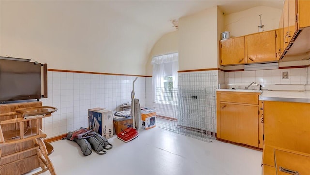 kitchen with a wainscoted wall, a sink, finished concrete floors, light countertops, and lofted ceiling