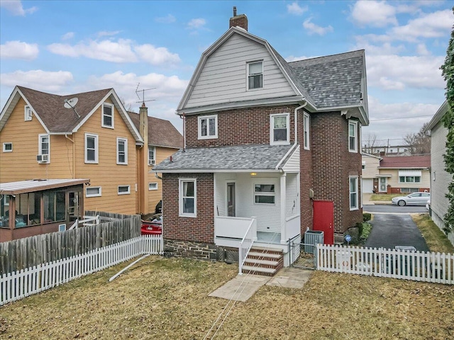 rear view of property featuring brick siding, a gambrel roof, fence private yard, roof with shingles, and a chimney