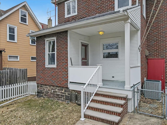 view of exterior entry featuring brick siding, cooling unit, a chimney, and fence