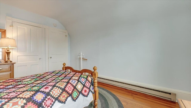 bedroom with vaulted ceiling, a baseboard heating unit, and wood finished floors