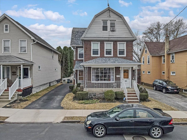 dutch colonial with a gambrel roof, brick siding, covered porch, and roof with shingles