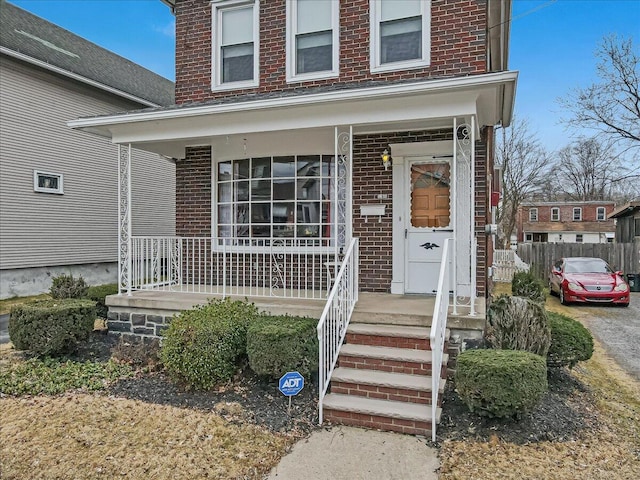 property entrance featuring brick siding, a porch, and fence