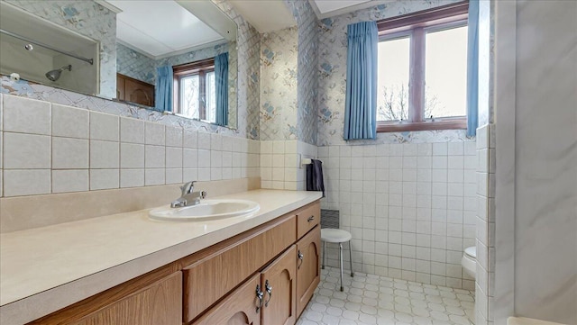 bathroom featuring vanity, wallpapered walls, wainscoting, tile walls, and toilet