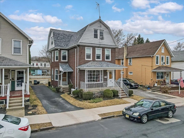 view of front of property featuring a gambrel roof, roof with shingles, a porch, and brick siding