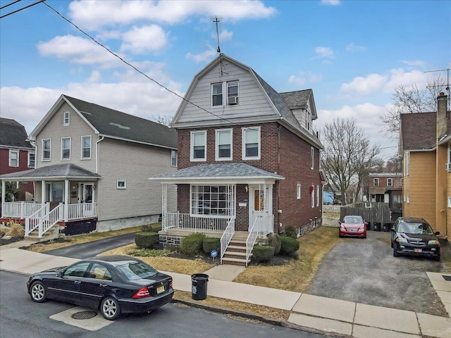 view of front of house with aphalt driveway, a gambrel roof, brick siding, and covered porch