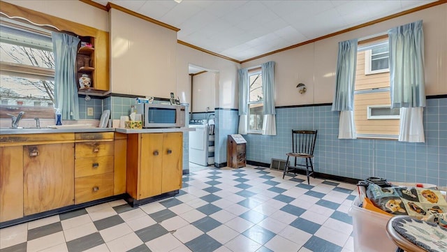 kitchen with ornamental molding, a sink, stainless steel microwave, light countertops, and light floors