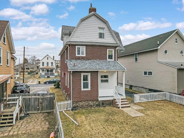 back of house with a gambrel roof, brick siding, a fenced backyard, and a chimney