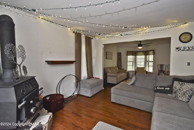 living area with a ceiling fan, a wood stove, and wood finished floors