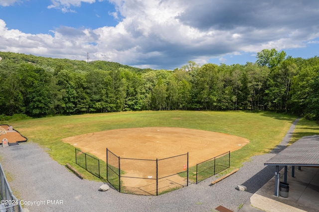 view of community with an enclosed area, a wooded view, and a lawn