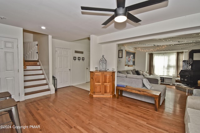 living room with stairs, a ceiling fan, and wood finished floors