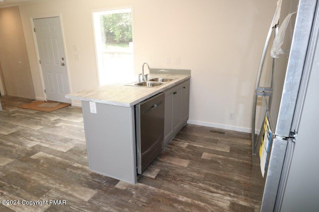 kitchen with a sink, a peninsula, appliances with stainless steel finishes, and dark wood finished floors