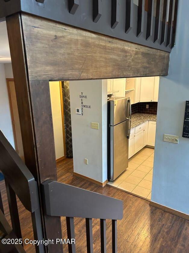 kitchen featuring white cabinetry, light wood-type flooring, backsplash, and stainless steel refrigerator