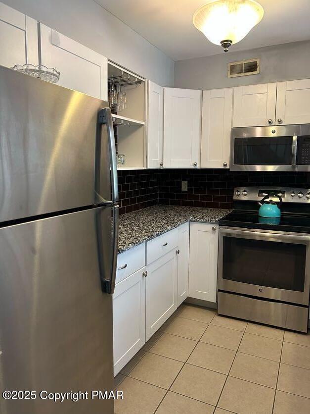 kitchen featuring visible vents, stainless steel appliances, dark stone counters, white cabinets, and decorative backsplash