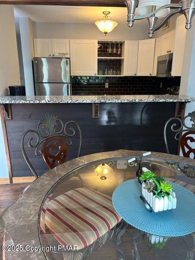 kitchen with stainless steel appliances, white cabinetry, light stone countertops, and tasteful backsplash