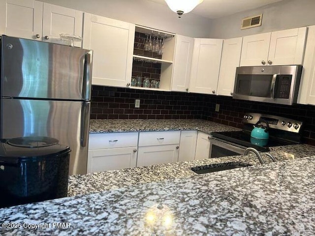 kitchen with decorative backsplash, stainless steel appliances, white cabinets, and stone counters