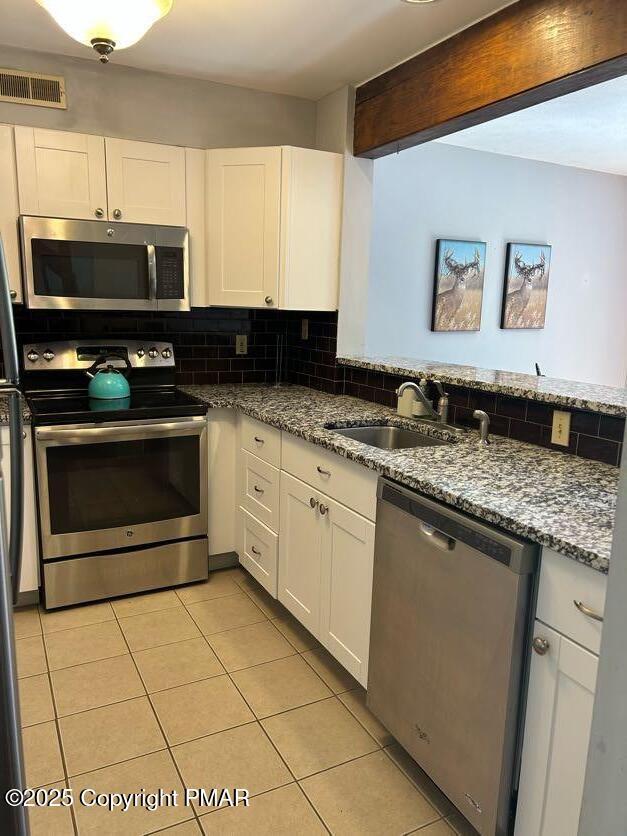 kitchen featuring visible vents, a sink, white cabinetry, stainless steel appliances, and decorative backsplash