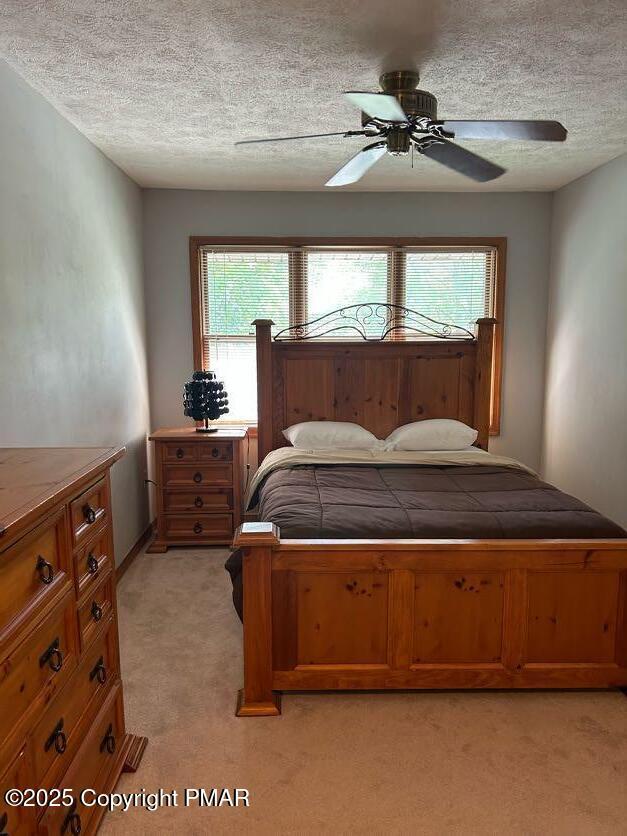 bedroom with ceiling fan, light colored carpet, and a textured ceiling