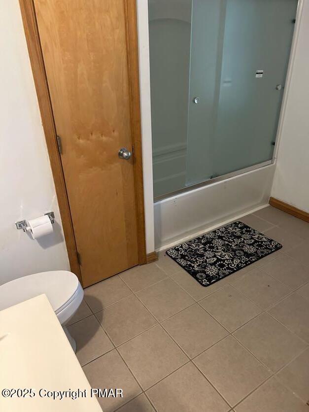 full bath featuring tile patterned floors, toilet, enclosed tub / shower combo, and baseboards