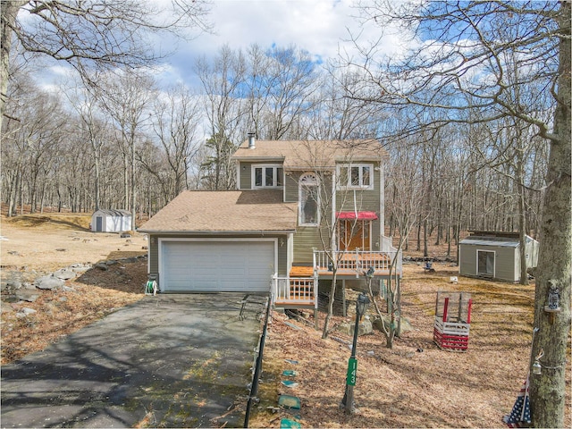 view of front of home featuring an outbuilding, a shed, driveway, and roof with shingles