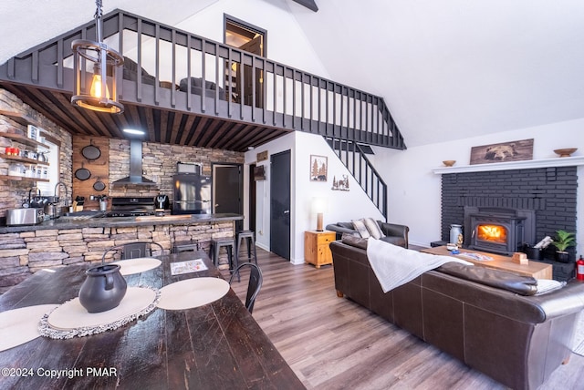 living area featuring a wood stove, high vaulted ceiling, stairway, and wood finished floors