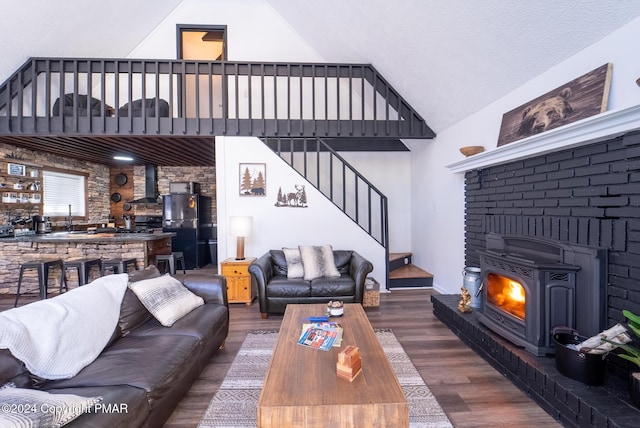 living area with a wood stove, stairs, high vaulted ceiling, and wood finished floors