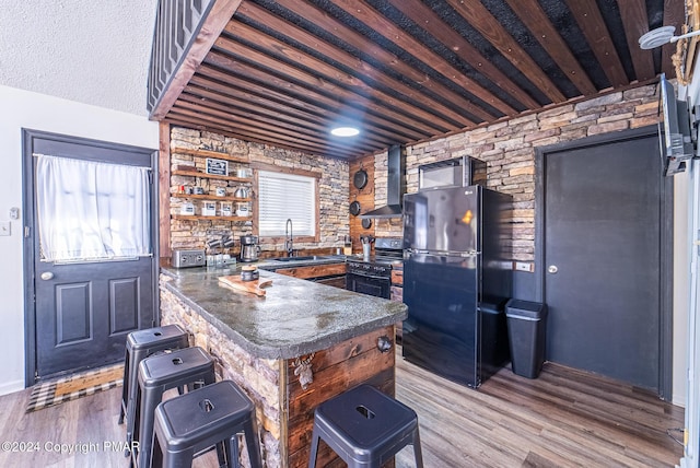 kitchen with wood finished floors, a sink, freestanding refrigerator, wall chimney exhaust hood, and dark countertops