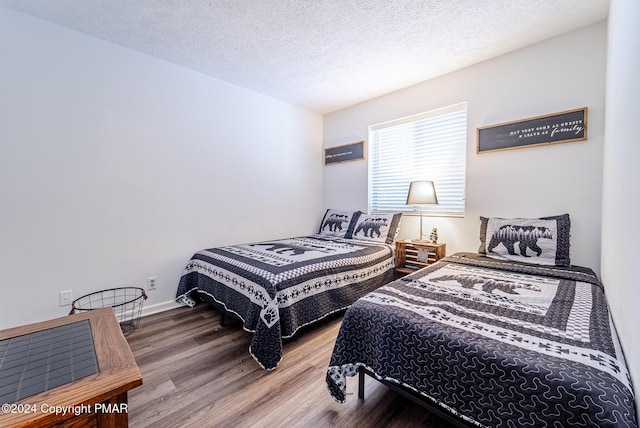 bedroom with a textured ceiling, baseboards, and wood finished floors