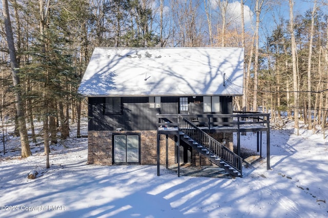 snow covered property featuring stairs, a deck, and brick siding