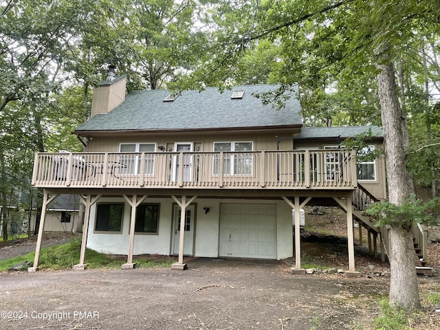 rear view of house with a deck, roof with shingles, aphalt driveway, and a chimney