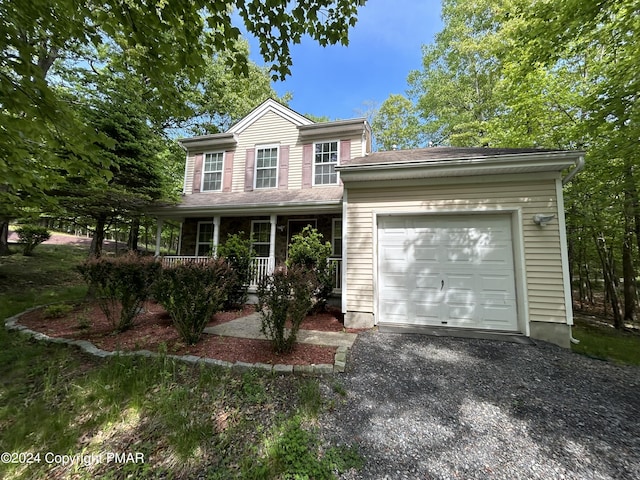 colonial home with gravel driveway, a garage, and a porch