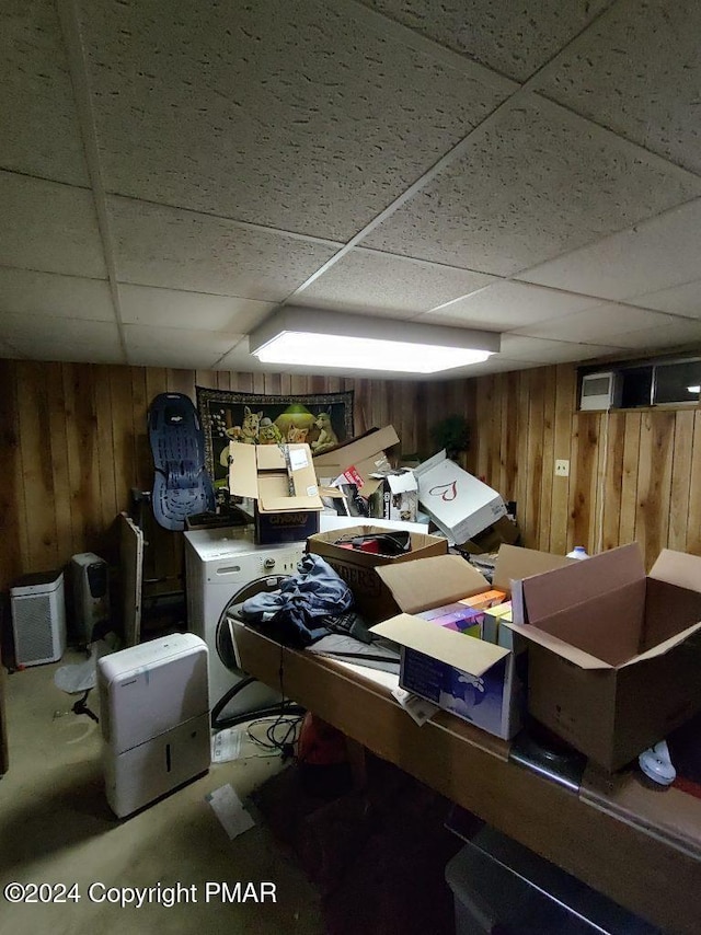 finished basement featuring wooden walls, washer / clothes dryer, and a paneled ceiling