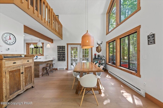 dining area with light wood-type flooring, a baseboard radiator, a towering ceiling, and baseboards