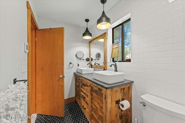 bathroom with double vanity, a sink, toilet, and tile walls